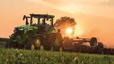 Traktor 8R von John Deere auf dem Feld bei Sonnenuntergang