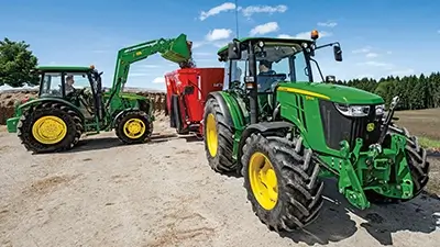 2 Traktoren der Serie 5M von John Deere auf dem Hof, kippen Sand in Mulde