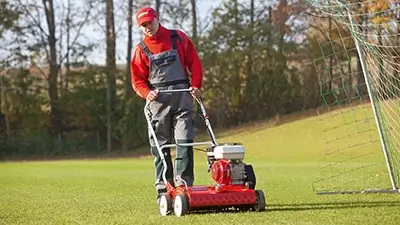 Mann beim Rasenmähen auf Fußballplatz