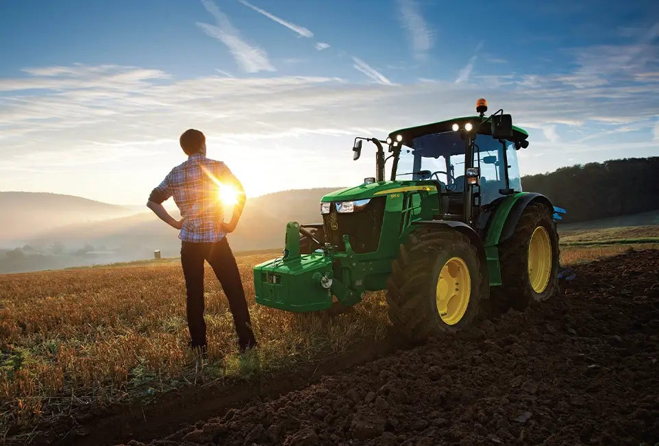 Mann vor Trecker im Sonnenaufgang