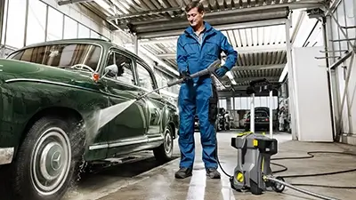 Mann in Waschanlage reinigt Auto mit Kärcher-Gerät