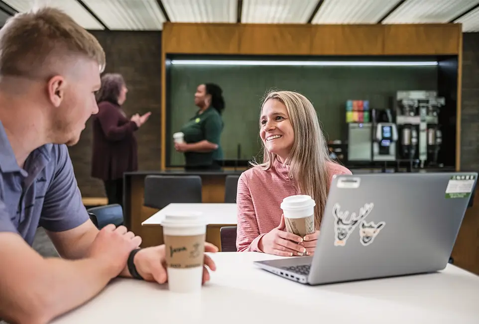 Menschen, die an einem Tisch in einer Pausenecke sitzen und sich mit Kaffeebechern in der Hand unterhalten